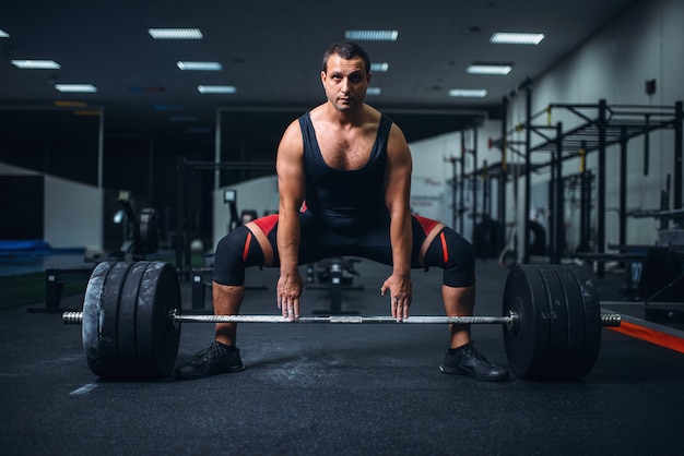 Male powerlifter preparing deadlift a barbell in gym.