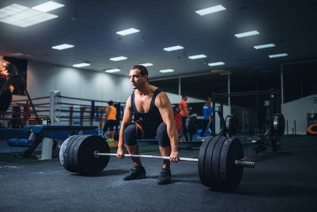 Powerlifter maschio che avvia lo stacco da terra un bilanciere in palestra.