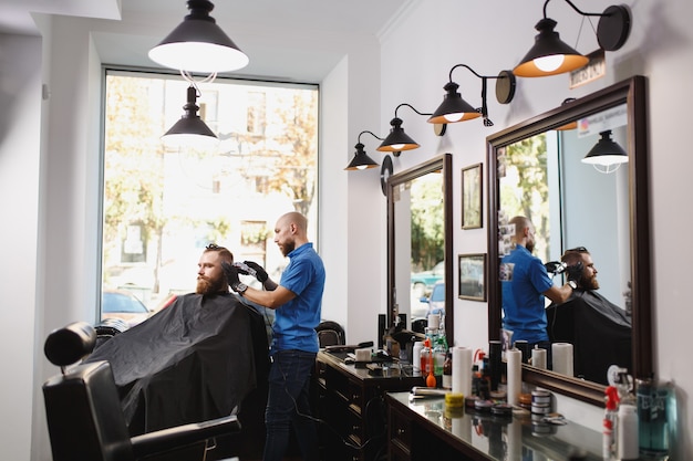 Male professional hairdresser serving client by clipper