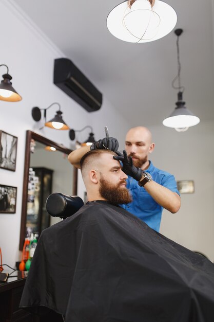 Male professional hairdresser serving client, shaving thick big beard straight razor