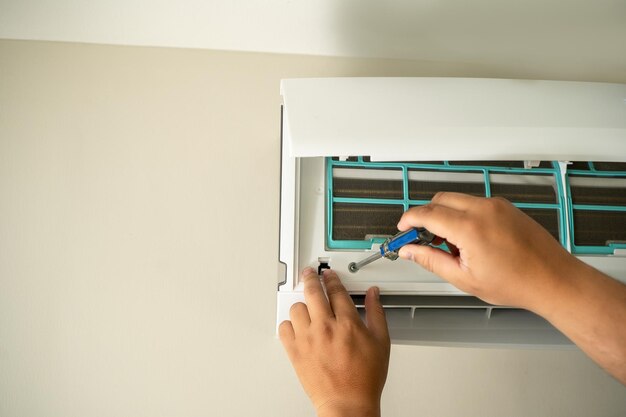male professional technician fixing an electrician repairs an air conditioner indoors removing air filter repairing hot temperatures
