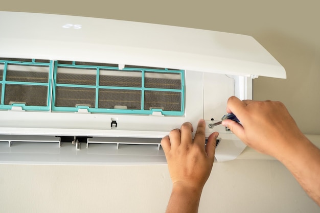 male professional technician fixing an electrician repairs an air conditioner indoors removing air filter repairing hot temperatures