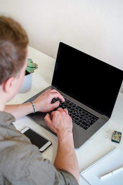 男性プログラマーは、明るいオフィスのノートパソコンの画面の前で、または自宅から離れた場所で作業します