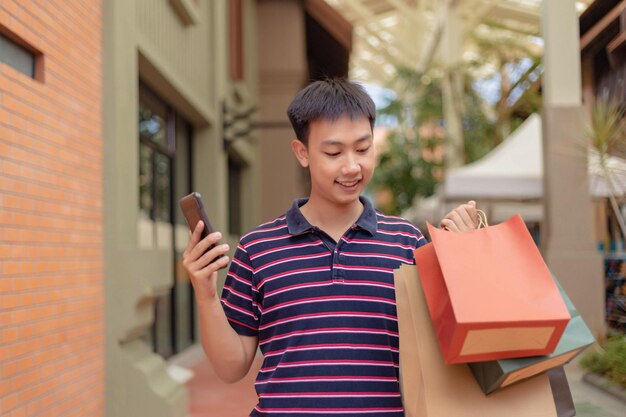 Male purchaser who carries his smartphone grinning cheerfully\
after buying a lot of goods