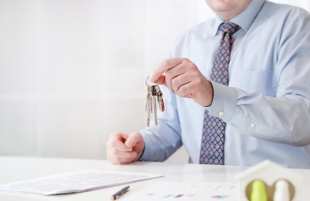 A male realtor holds the keys to the apartment in his hands There is a contract on the table