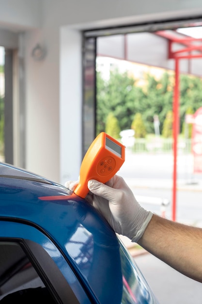 Male repair worker examining car paint with equipment in repair shop