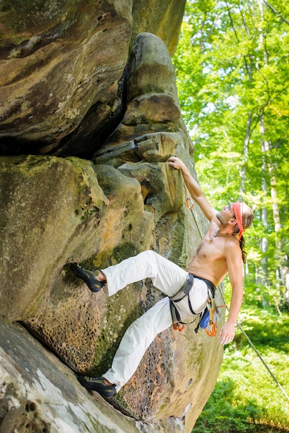 Male rock climber climbing with rope on a rocky wall