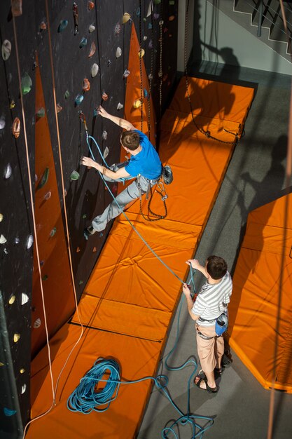 Male rock-climber practicing climbing on rock wall indoors