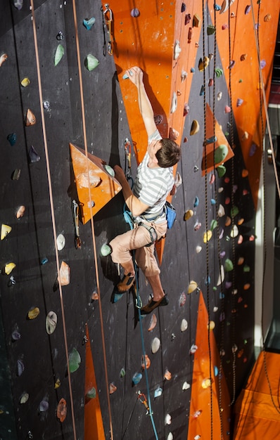 Male rock-climber practicing climbing on rock wall indoors