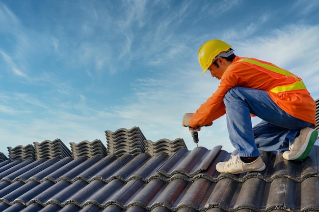 Lavoratori edili maschi dell'installatore del tetto sul lavoro del tetto utilizzare una punta da trapano per fissare le viti del tetto delle tegole di ceramica o di cemento nel cantiere