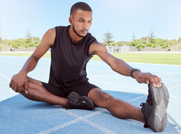 Male runner doing stretching exercises while sitting on sports track Determined young male athlete sitting alone and warming up his muscles before going for a run Fitness man preparing for a race