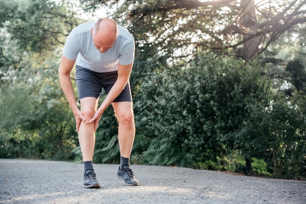 膝を抱えてランナーの膝の怪我に苦しんでいる男性ランナー