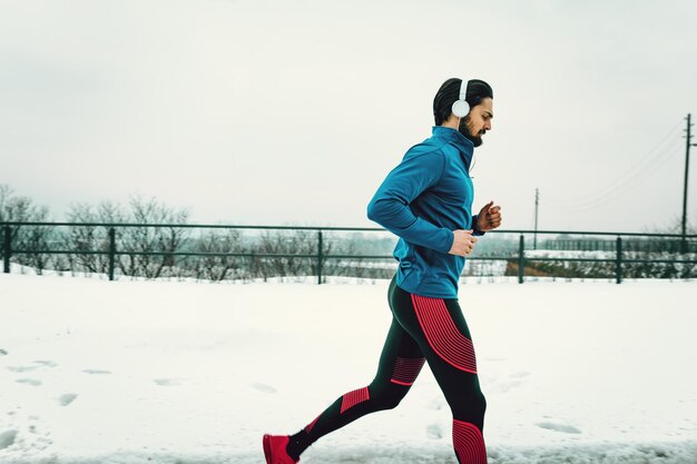 外で冬のトレーニング中に公共の場所で走っている彼の耳にヘッドフォンを持った男性ランナー。コピースペース。