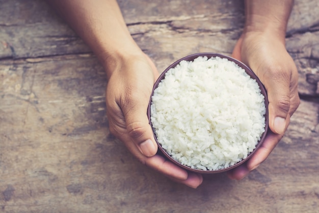 male's hand holding a bowl with cooked rice on old wooden table