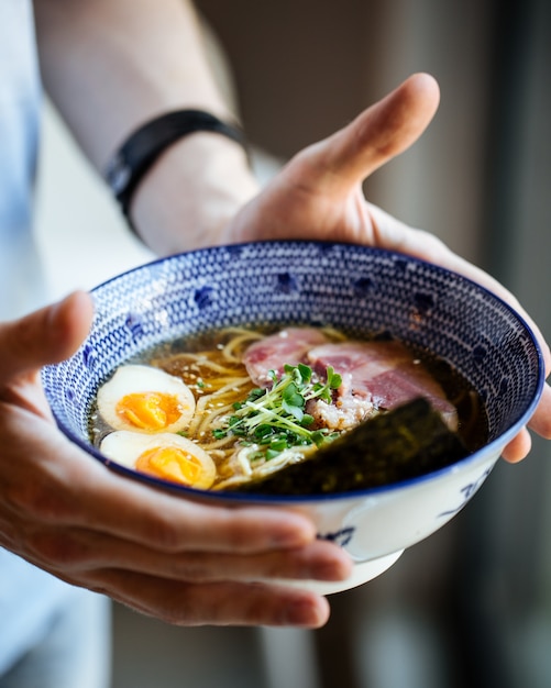 Male's hands holding asian japanese shio ramen noodle soup with eggs