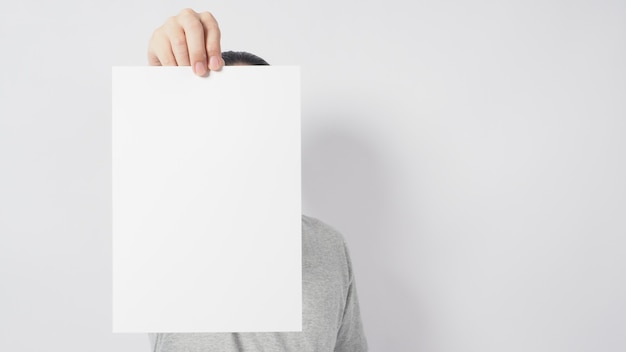 Male's hands is holding the A4 paper and wear gray t shirt and standing on white background.