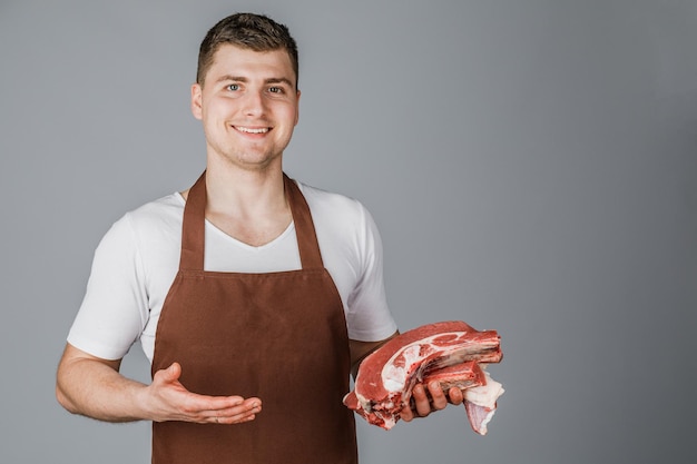 A male salesman or cook holds raw meat in his hands and shows it on a gray background.