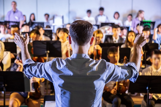 男性の学校の指導者が学校のコンサートで音楽を演奏するために彼の学生バンドを導く