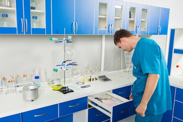 Ученый-мужчина в униформе что-то ищет в ящиках в лаборатории. Концепция здравоохранения и биотехнологии