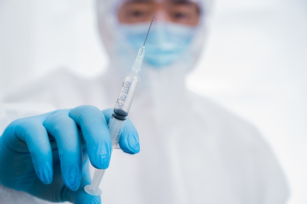 A male scientist wearing blue gloves and a protective suit holding a Covid-19 vaccine.