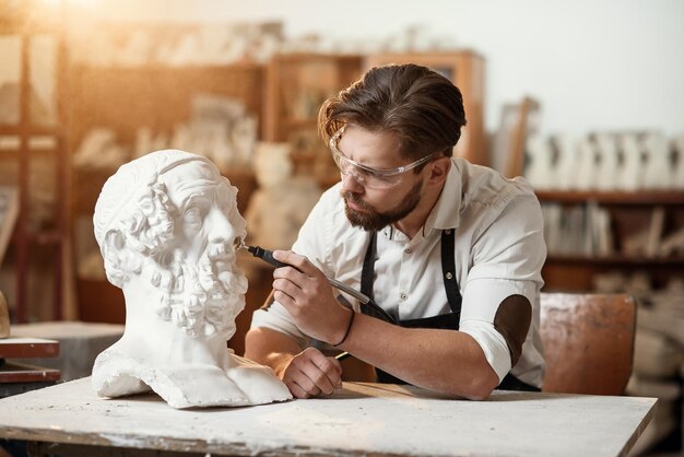 Фото Мужчина-скульптор ремонтирует гипсовую скульптуру женской головы на рабочем месте в творческом центре