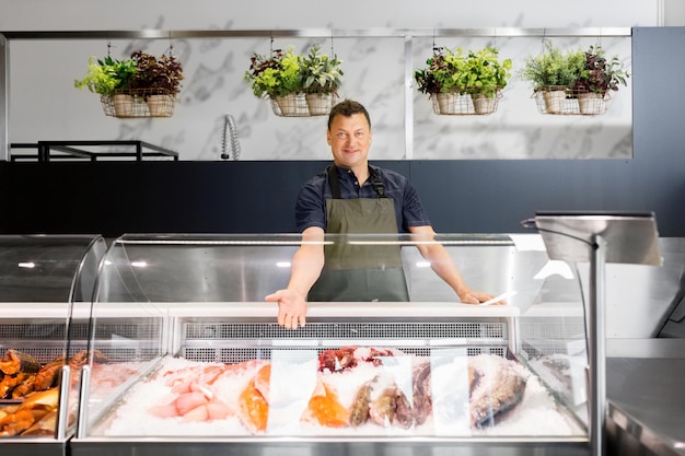 Photo male seller showing seafood at fish shop fridge