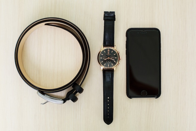 Male set - men's  black leather belt on trousers, wristwatch and phone close up. set of stylish men's accessories. groom accessories. details of business man's clothing