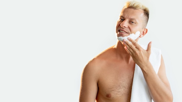 Male shaving Cosmetic product Grooming hygiene Morning routine Portrait of satisfied shirtless man applying white shaving foam on face smiling isolated on light copy space advertising background