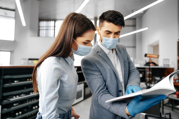 Assistente di negozio maschio in maschera che mostra il catalogo degli elettrodomestici del cliente femminile