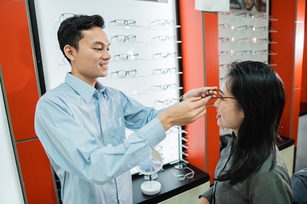 The male shop assistant puts glasses on to the female customer while at the optician