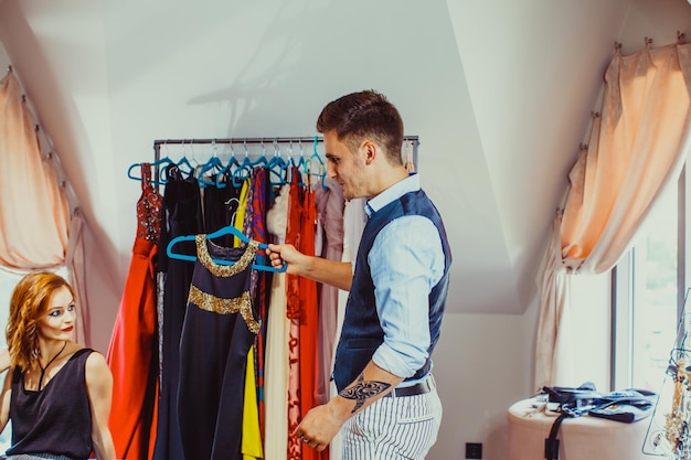Assistente di negozio maschio e giovane donna che sceglie l'abito da sera nella boutique di moda. concetto di affari di moda