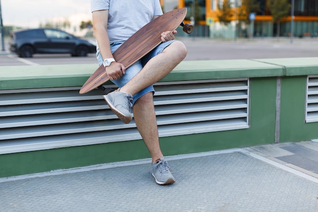 Photo male in shorts and grey sneakers holding longboard in hands wooden longboard urban area