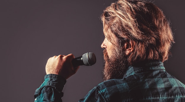 Canto maschile con microfoni. uomo con la barba che tiene un microfono e canta. l'uomo barbuto al karaoke canta una canzone in un microfono.