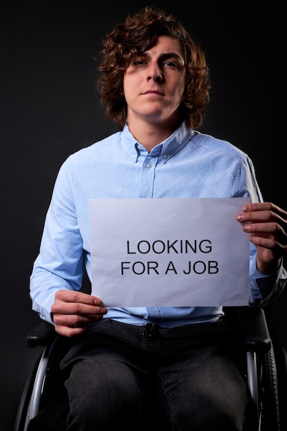 Male sits with job search paper seriously, looking for a job. isolated black wall