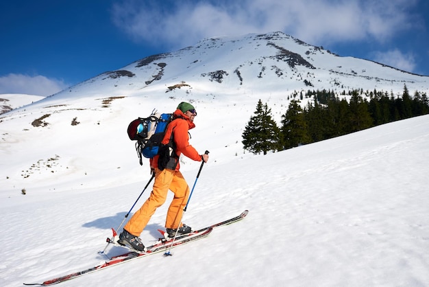 Male skiclimber climbing a snowy ridge in background the peaks of mountains at sunny day