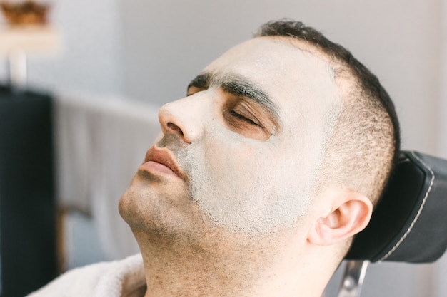 Male skin care in a beauty salon. Applying clay cleansing mask on a man's face