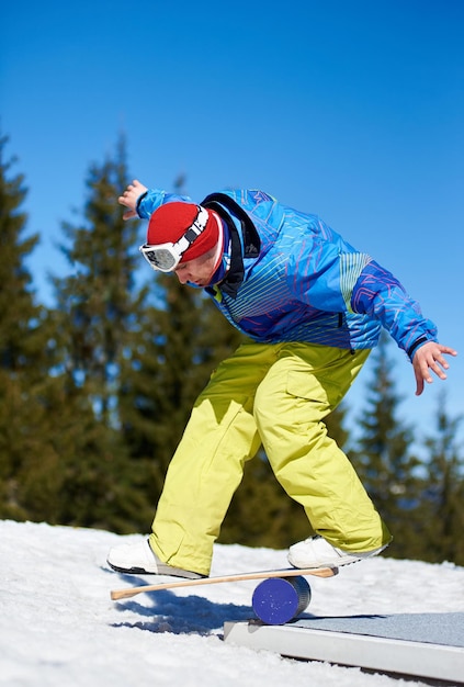 Male snowboarder balancing on snowboard in white snow on background of blue sky and spruce trees