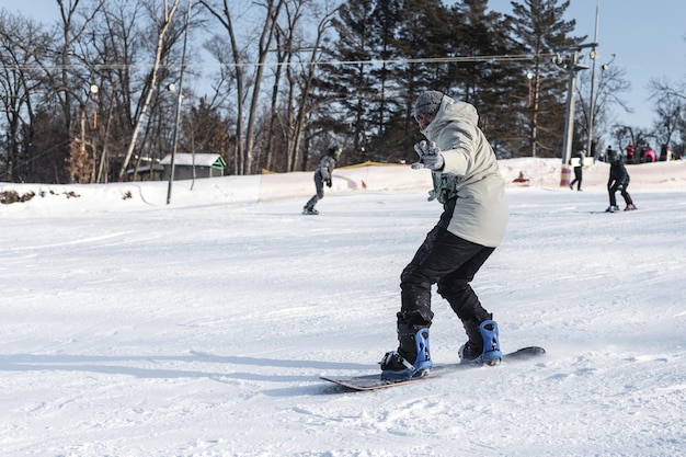 A male snowboarder is snowboarding down a snowy slope looking at the camera and waving his hand