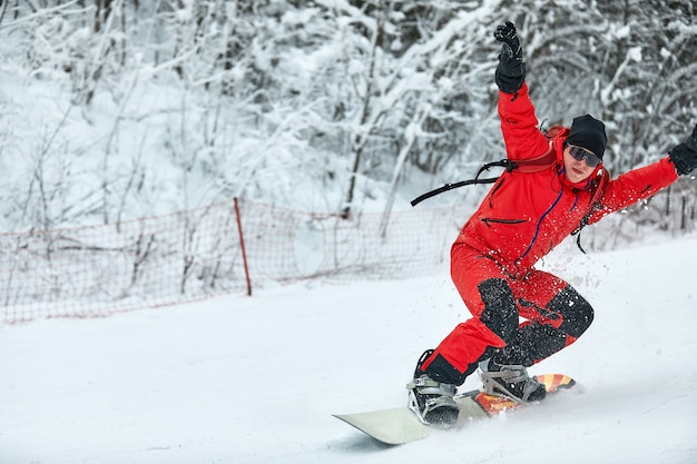 赤いスーツを着た男性のスノーボーダーは、スノーボード、スキー、スノーボードのコンセプトで雪の丘に乗ります。