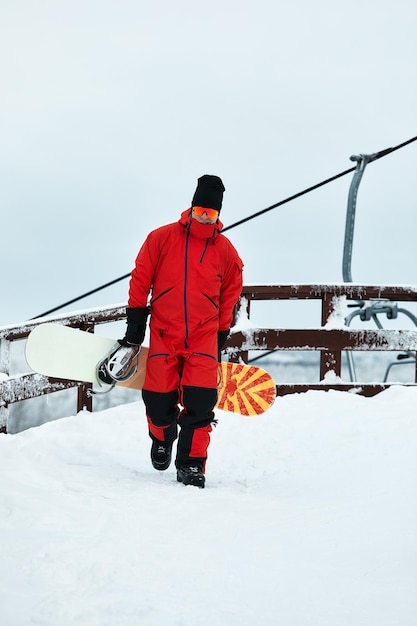 Male snowboarder in a red suit walking on the snowy hill with snowboard Skiing and snowboarding concept