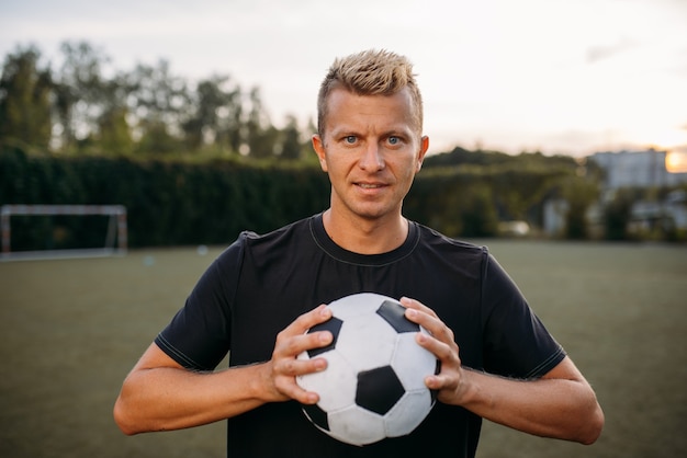 Male soccer player holding ball in hands on the field. Footballer on outdoor stadium, workout before game, football training