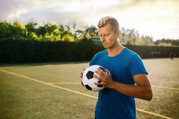 フィールドで手にボールを持つ男性のサッカー選手。屋外スタジアムでのサッカー選手、試合前のトレーニング、サッカーのトレーニング