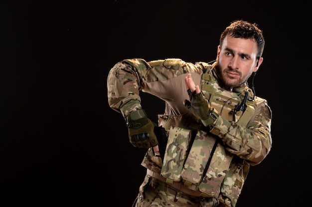 Male soldier in camouflage aiming gun on black wall