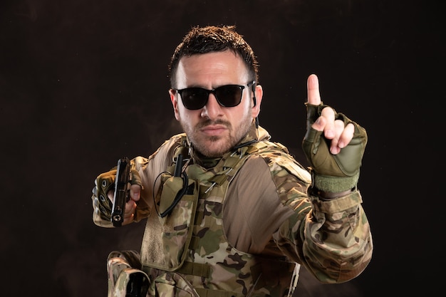 Male soldier in camouflage fighting with gun on dark wall