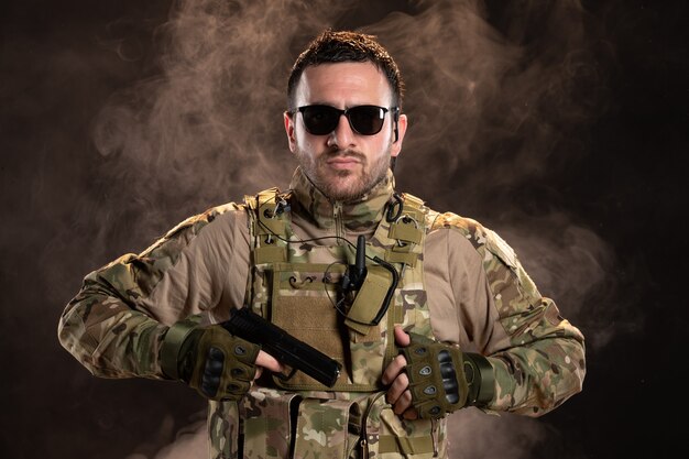 Male soldier in camouflage holding gun on dark wall