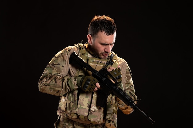 Мужчина-солдат в камуфляже держит пулемет на черной стене