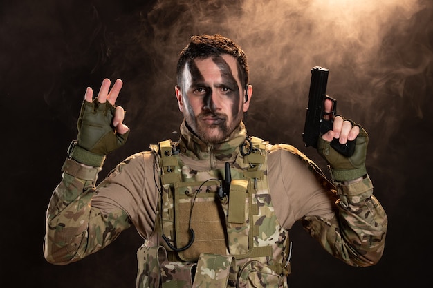 Male soldier in camouflage with gun on a smoky dark wall