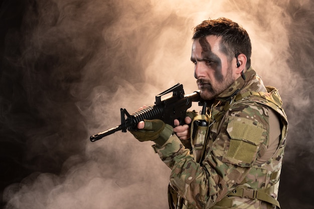 Male soldier in camouflage with machine gun on dark wall