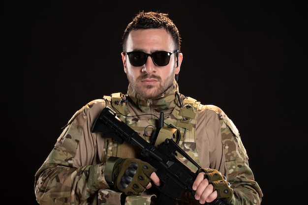 Male soldier in camouflage with machine gun on dark wall