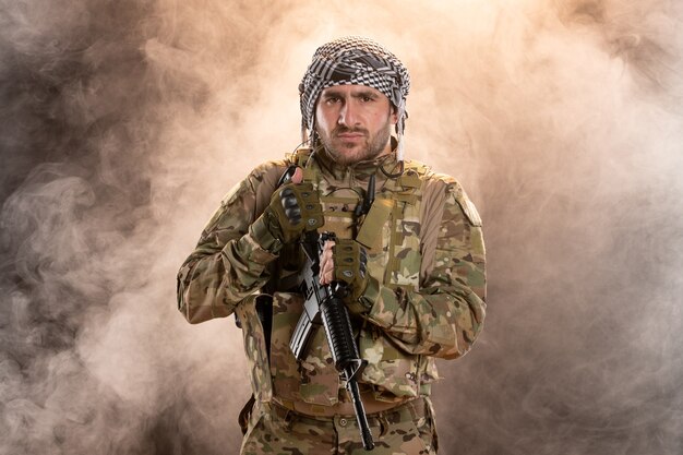 Male soldier in camouflage with machine gun on smoky wall